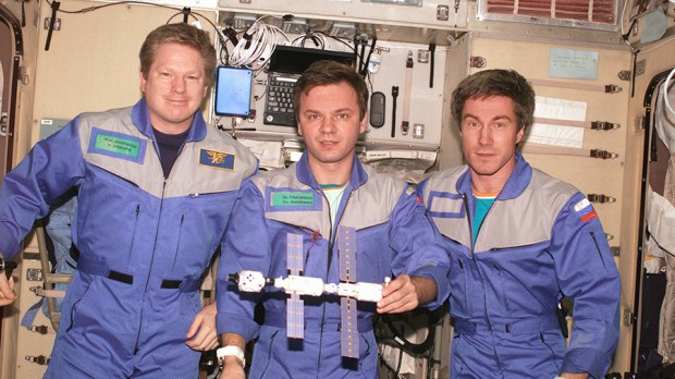 Expedition 1, the first space station crew, poses inside the Zvezda service module with a model of the young International Space Station. Pictured in December 2000 (from left) are Commander William Shepherd and Flight Engineers Yuri Gidzenko and Sergei Krikalev. - Via NASA